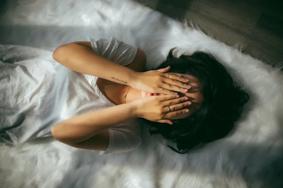 両掌で顔を覆った女性が寝転んでいる写真